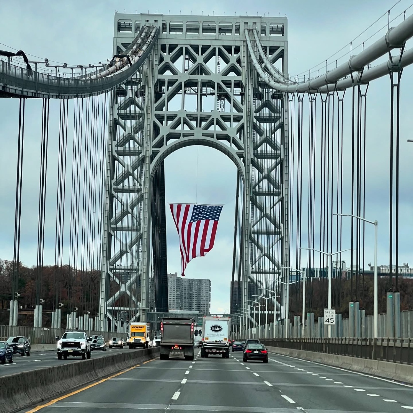 A freight truck crossing the George Washington Bridge, a large American flag hung from the tower