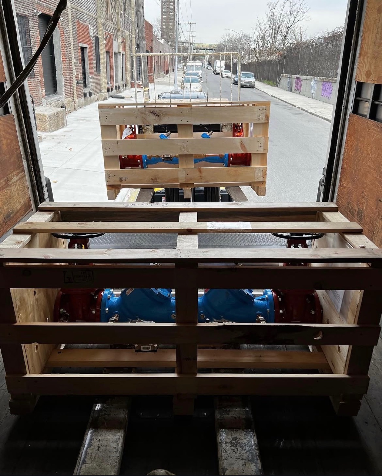 Crated industrial valves lowered on a liftgate at a New York City job site